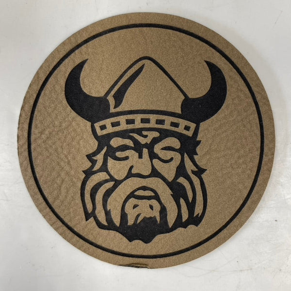 A circular brown Northmen Leather Patch by Sanderson Lacrosse features a black Viking head with a horned helmet and bushy beard, set against a plain background. Available as single or multipack—great for unique lacrosse gifts.