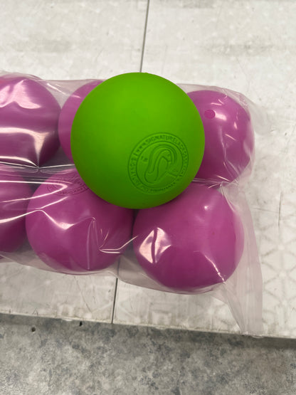 A sealed plastic pack of Sanderson Lacrosse Warrior Lacrosse Balls in purple with one bright green ball on top, each featuring a circular logo, sits on a light tiled floor.