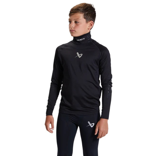 A boy faces left in a black Bauer LS Cut-Resistant Neck Protect Base Layer—long-sleeve athletic top and matching leggings with white Bauer logos—designed for youth hockey, shown against a plain white background.