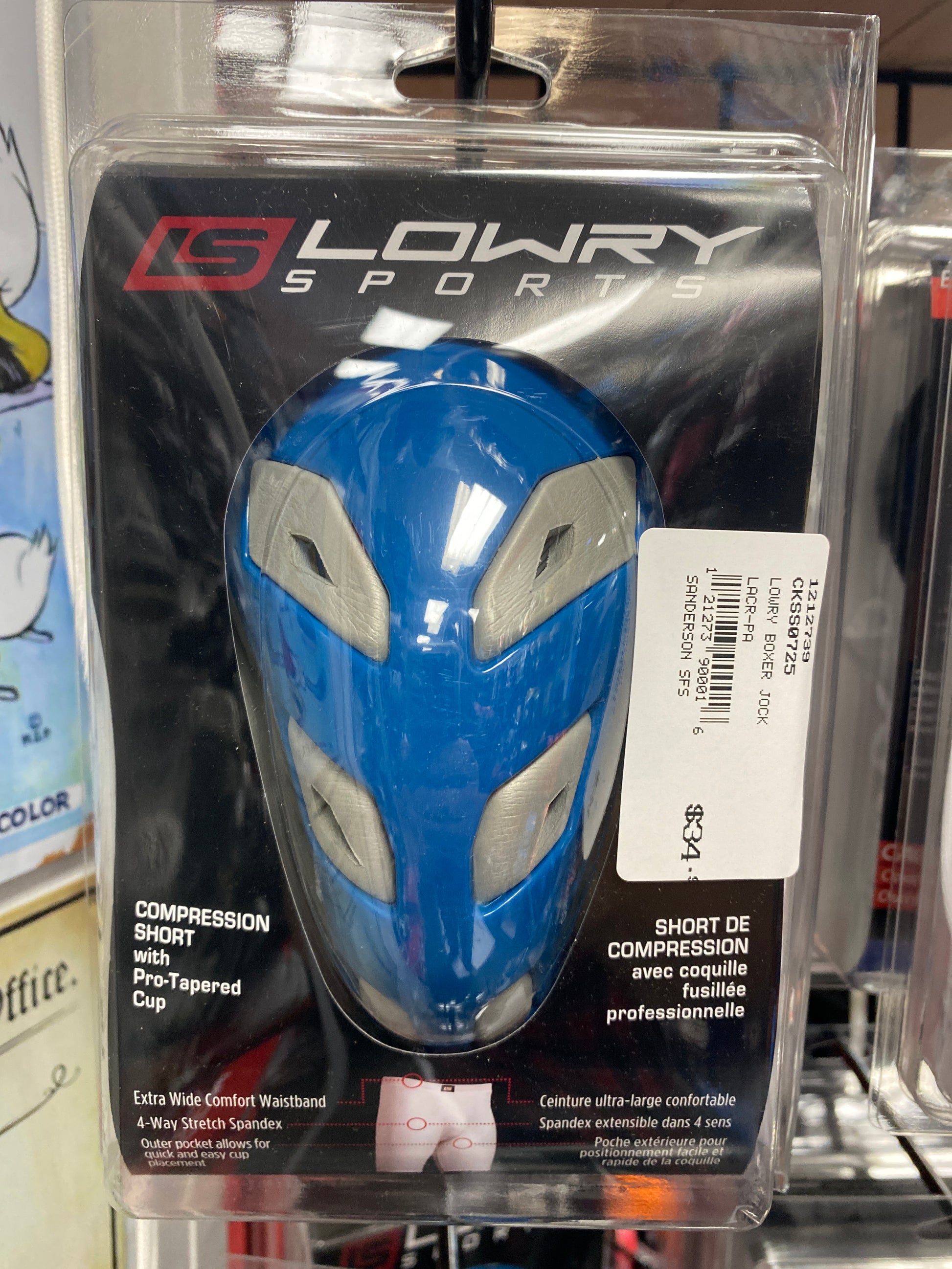 A SafeTgard Lowry Athletic Support/Jocks Boxer with Cup package in blue and gray is displayed on a store shelf, featuring a pro-tapered protective cup. A white price label is attached to the upper right of the package.