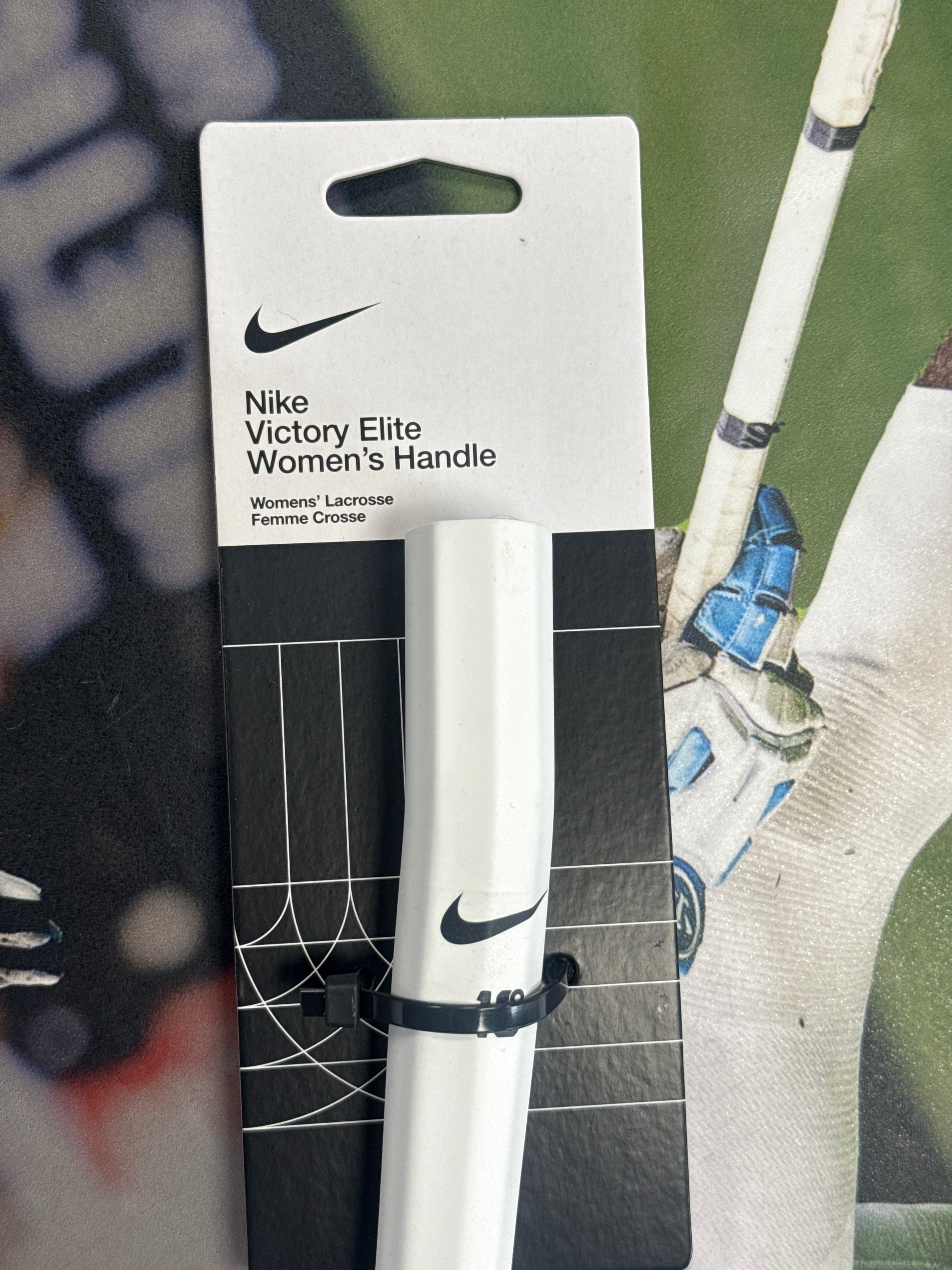 The Nike Victory Elite Women’s Lacrosse Shaft, by Nike, is displayed in black and white packaging with the logo and held securely by a black zip tie, emphasizing its lightweight, elite design.