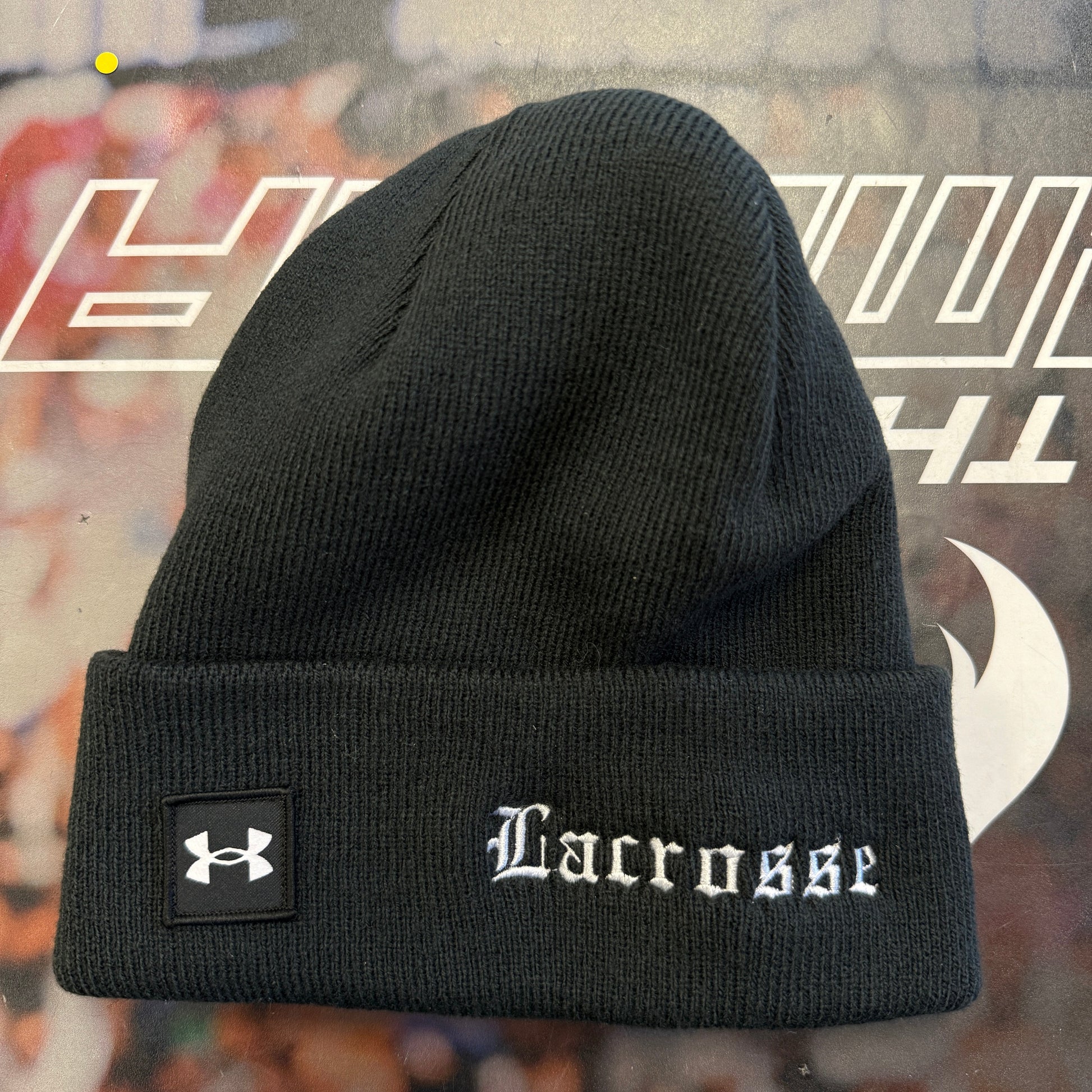 Black beanie with 'Lacrosse' and Under Armour logo on a blurred background
