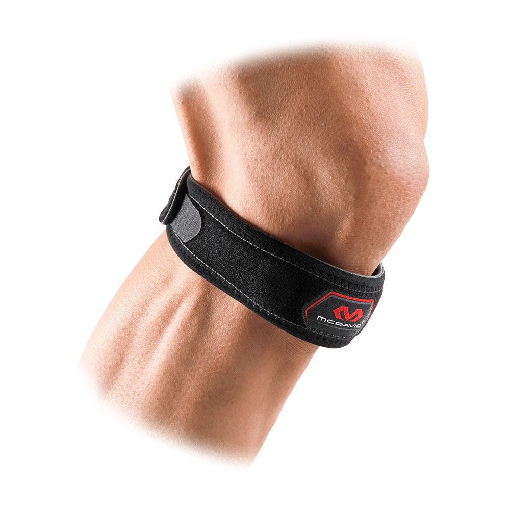 A close-up of a person's elbow wearing the McDavid Knee Strap/Patella, a black neoprene strap with Velcro closure and red and white McDavid logo, designed for patellar tendonitis relief. One size fits most.