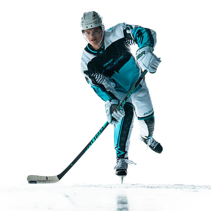 A hockey player in a white and teal uniform skates forward on the ice, gripping a Bauer Pulse Hockey Stick by Bauer with mid-kick flex, focused ahead against a white background.