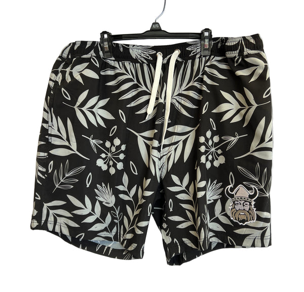 The Sanderson Lacrosse Northmen Lacrosse Bardown Drawstring Swim Shorts feature a white tropical leaf pattern and Viking face patch—ideal for the beach after practice or stringing supplies. Hanging on a plastic hanger.