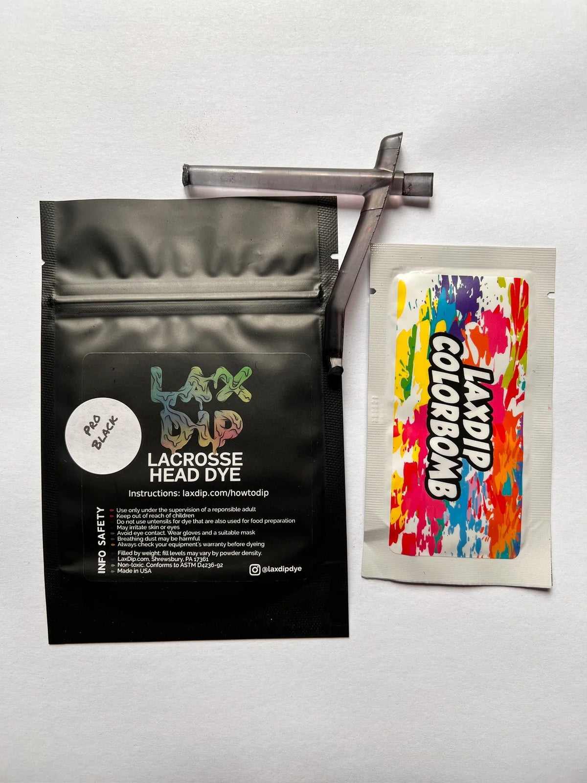 A resealable black pouch labeled LaxDip Colorbombs by LaxDip, with a stir stick and a vibrant color packet—everything you need to customize your lacrosse stick with bold, vibrant colors.