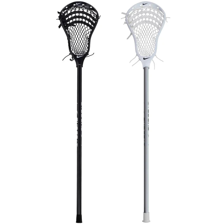 Two Nike Surge LT Complete Attack Lacrosse Sticks, one black and one white with mesh pockets and a Nike logo, stand upright against a white background. This stick is ideal for beginners looking for a quality lacrosse experience.